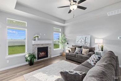 Living area featuring a tray ceiling, wood finished floors, a fireplace, and ceiling fan