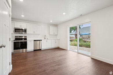 Kitchen featuring appliances with stainless steel finishes, dark wood-style floors, light countertops, white cabinets, and recessed lighting