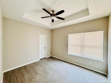 Empty room with a raised ceiling, a ceiling fan, and wood finished floors