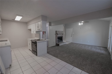 Kitchen with light colored carpet, black range with electric cooktop, light tile patterned floors, a brick fireplace, and light countertops