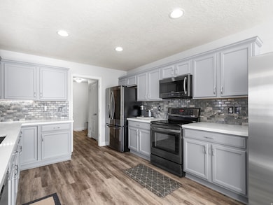 Kitchen featuring gray cabinets, decorative backsplash, stainless steel appliances, a textured ceiling, and light wood-style flooring
