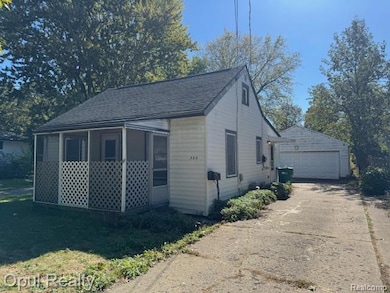 View of side of home with roof with shingles, a sunroom, an outbuilding, a detached garage, and a yard