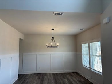 Unfurnished dining area featuring a decorative wall, wainscoting, dark wood-style flooring, and a chandelier