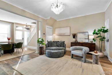 Living area featuring stairs, ornamental molding, a chandelier, ornate columns, and wood finished floors
