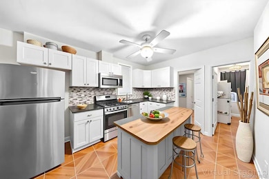 Kitchen featuring stainless steel appliances, backsplash, a center island, white cabinets, and a kitchen breakfast bar