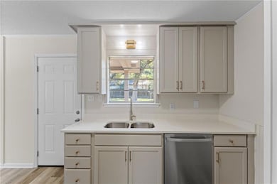 Kitchen featuring stainless steel dishwasher, light wood-type flooring, light stone countertops, a textured ceiling, and ornamental molding