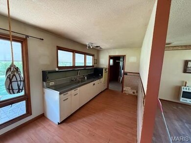 Kitchen featuring light wood-style floors, a textured ceiling, white cabinetry, dark countertops, and heating unit