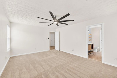 Spacious bedroom featuring plush neutral carpeting, abundant natural light from the window, and a modern ceiling fan for comfort. Offers private access to an en-suite bathroom, making it a perfect retreat.