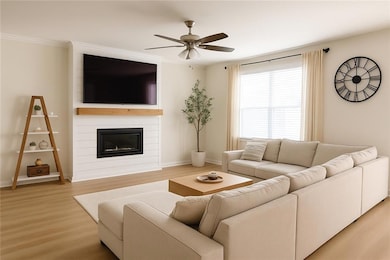 Living area featuring light wood-style floors, ceiling fan, a large fireplace, baseboards, and ornamental molding