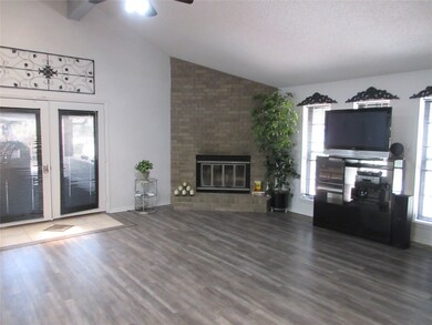 Unfurnished living room featuring vaulted ceiling, plenty of natural light, a brick fireplace, a ceiling fan, and wood finished floors