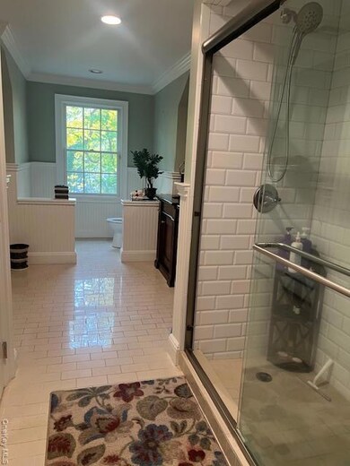 Bathroom with a wainscoted wall, crown molding, a shower stall, light tile patterned floors, and recessed lighting