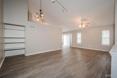 Unfurnished living room with dark wood-style floors, track lighting, a ceiling fan, and a chandelier
