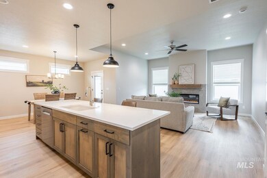 Kitchen featuring stainless steel dishwasher, light wood-type flooring, a glass covered fireplace, a ceiling fan, and a kitchen island with sink