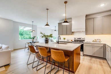 Kitchen featuring gray cabinetry, stainless steel range with electric stovetop, decorative light fixtures, light wood-type flooring, and an island with sink