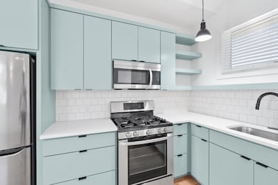 Kitchen with open shelves, appliances with stainless steel finishes, hanging light fixtures, and backsplash