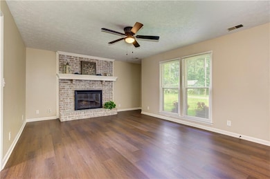 Unfurnished living room featuring dark wood-type flooring, a textured ceiling, ceiling fan, and a brick fireplace