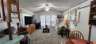 Living room with a textured ceiling, light carpet, ceiling fan, and vaulted ceiling