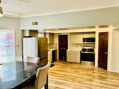 Kitchen featuring ornamental molding, stainless steel appliances, light wood-type flooring, decorative backsplash, and a textured ceiling