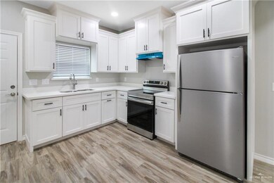 Kitchen with appliances with stainless steel finishes, a sink, under cabinet range hood, light countertops, and white cabinets