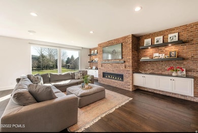 Living area with dark wood-type flooring, brick wall, a glass covered fireplace, and recessed lighting