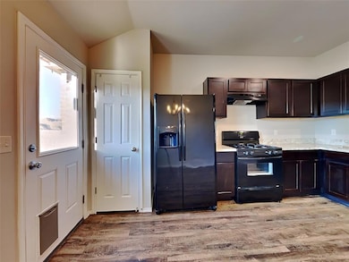Kitchen featuring refrigerator with ice dispenser, black gas stove, exhaust hood, light wood-style flooring, and light countertops