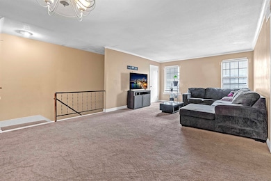 Living room featuring a chandelier, carpet floors, a textured ceiling, and ornamental molding