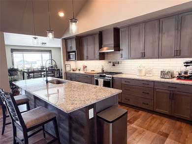 Kitchen featuring lofted ceiling, dark wood-style flooring, a kitchen bar, light stone counters, and wall chimney range hood