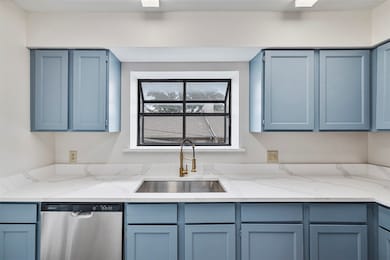 Kitchen with blue cabinetry, stainless steel dishwasher, and light stone counters