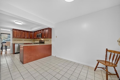 Kitchen with light stone counters, a peninsula, decorative backsplash, light tile patterned flooring, and appliances with stainless steel finishes