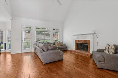 Living room featuring high vaulted ceiling, hardwood / wood-style floors, a brick fireplace, and a ceiling fan