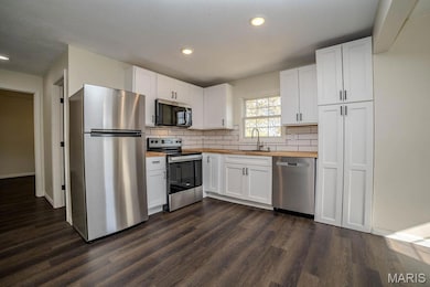 Kitchen featuring appliances with stainless steel finishes, decorative backsplash, white cabinets, wooden counters, and dark wood-style floors