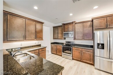 Kitchen with stainless steel appliances, light wood-type flooring, dark stone counters, and recessed lighting