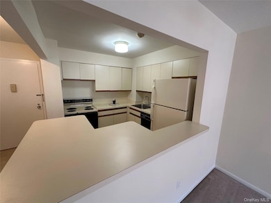 Kitchen with light countertops, white appliances, white cabinets, a peninsula, and light carpet