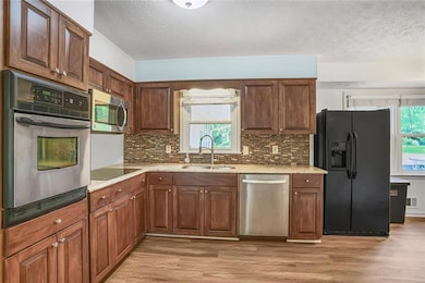 Kitchen with black appliances, a sink, light wood-style floors, a textured ceiling, and decorative backsplash