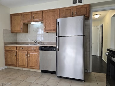 Kitchen featuring brown cabinetry, stainless steel appliances, tasteful backsplash, light countertops, and light tile patterned flooring