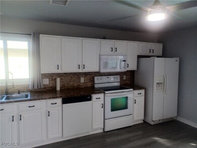 Kitchen featuring white appliances, white cabinets, dark wood finished floors, and decorative backsplash