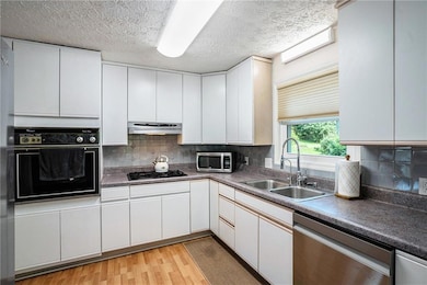 Kitchen with stainless steel appliances, light wood-type flooring, white cabinets, and a textured ceiling