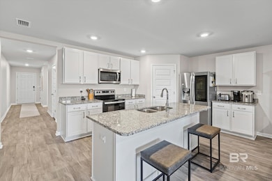 Kitchen with a kitchen bar, white cabinetry, stainless steel appliances, light stone countertops, and recessed lighting