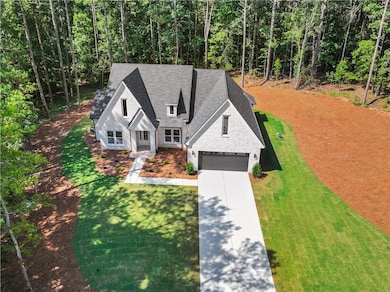 View of front of house with a garage, driveway, roof with shingles, a front lawn, and a wooded view