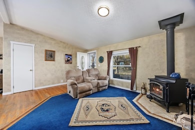 Living area with a wood stove, lofted ceiling, a textured ceiling, and wood finished floors