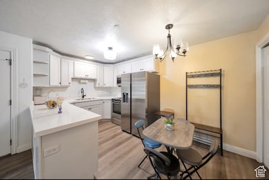 Kitchen featuring light countertops, open shelves, stainless steel appliances, light wood finished floors, and a textured ceiling