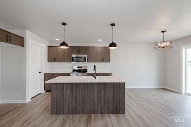 Kitchen with decorative light fixtures, light wood-style flooring, stainless steel appliances, a center island with sink, and modern cabinets