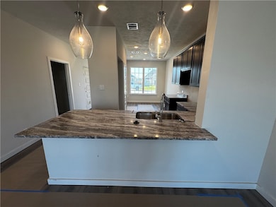 Kitchen with a peninsula, recessed lighting, dark stone countertops, pendant lighting, and dark wood finished floors