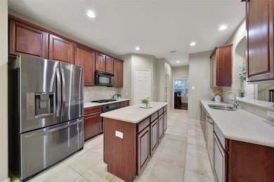 This modern kitchen features stainless steel appliances, rich wood cabinetry, and a central island. It has ample counter space, recessed lighting, and a tiled floor, creating a functional and inviting space for cooking and entertaining.