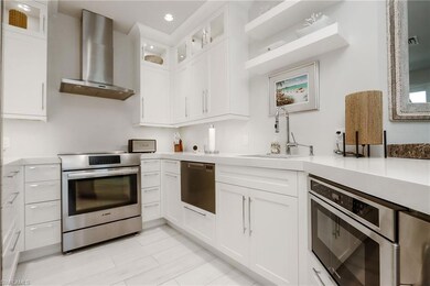 Kitchen featuring wall chimney exhaust hood, stainless steel appliances, light countertops, recessed lighting, and white cabinetry