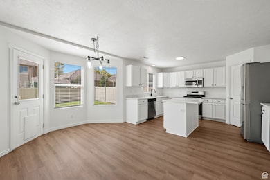 Kitchen featuring stainless steel appliances, a center island, light countertops, light wood-style floors, and a textured ceiling