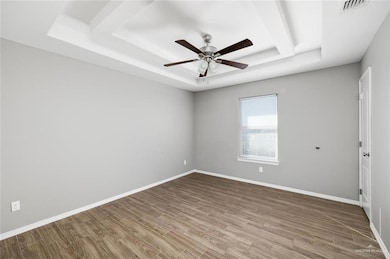 Spare room with a tray ceiling, wood finished floors, and ceiling fan