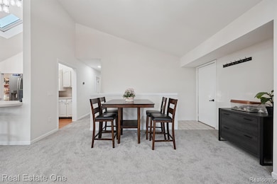 Dining room featuring a skylight, light colored carpet, and high vaulted ceiling