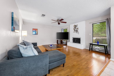 Living room with a textured ceiling, light wood finished floors, ceiling fan, and a brick fireplace