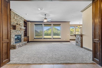 Unfurnished living room with a fireplace, crown molding, carpet, ceiling fan, and a chandelier